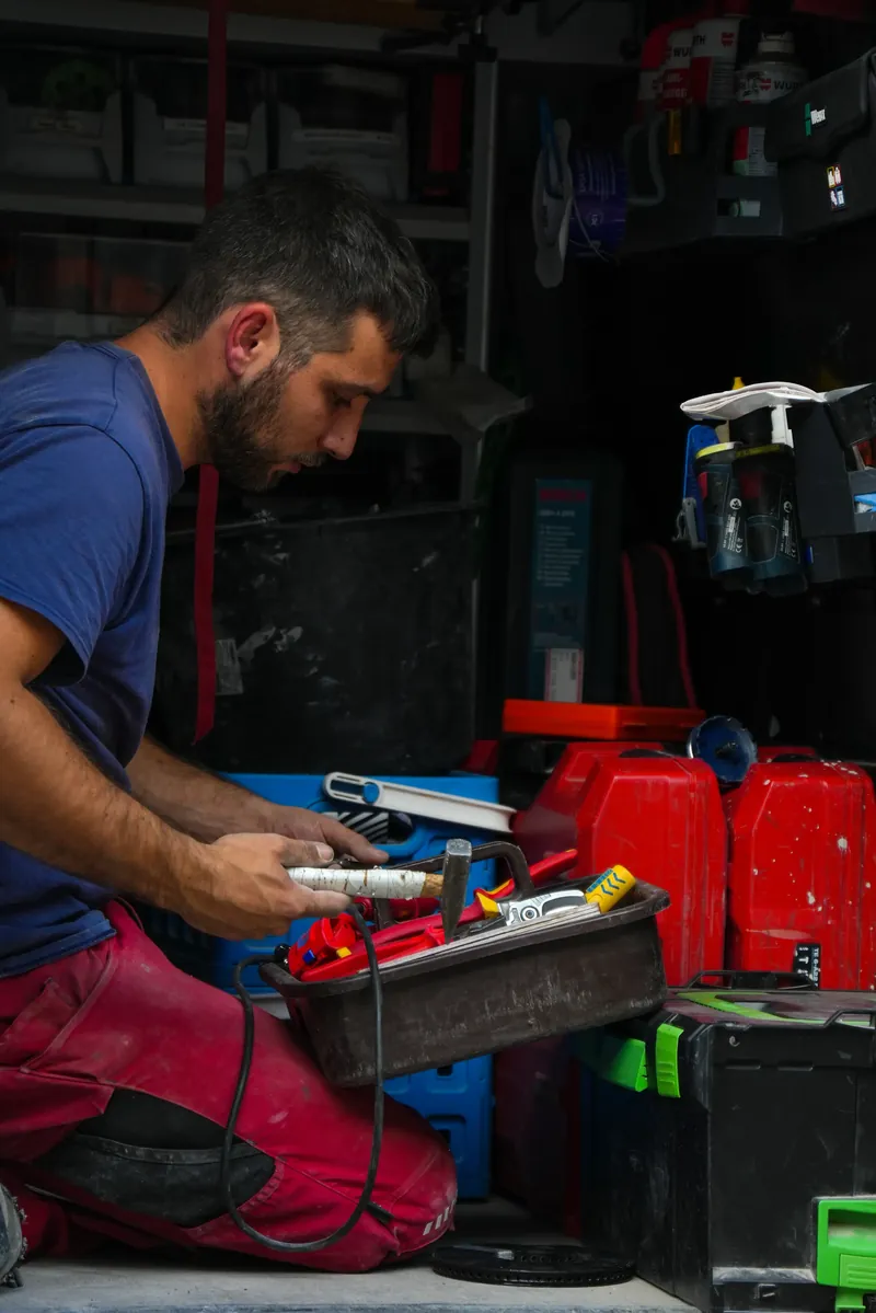 Mitarbeiter kniet im Firmenwagen und sortiert Werkzeug